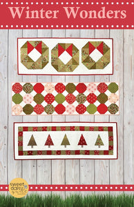 Quilt pattern with Christmas-themed designs on a wooden background, featuring the brand 'Sweet Daisy'.
