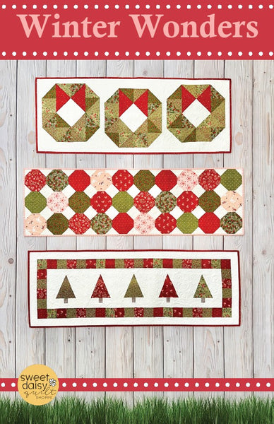 Quilt pattern with Christmas-themed designs on a wooden background, featuring the brand 'Sweet Daisy'.