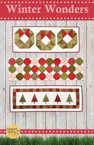 Quilt pattern with Christmas-themed designs on a wooden background, featuring the brand 'Sweet Daisy'.